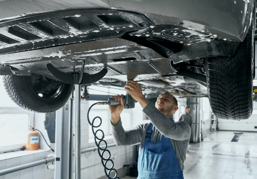 Competent mechanic in blue overalls repairing car suspension