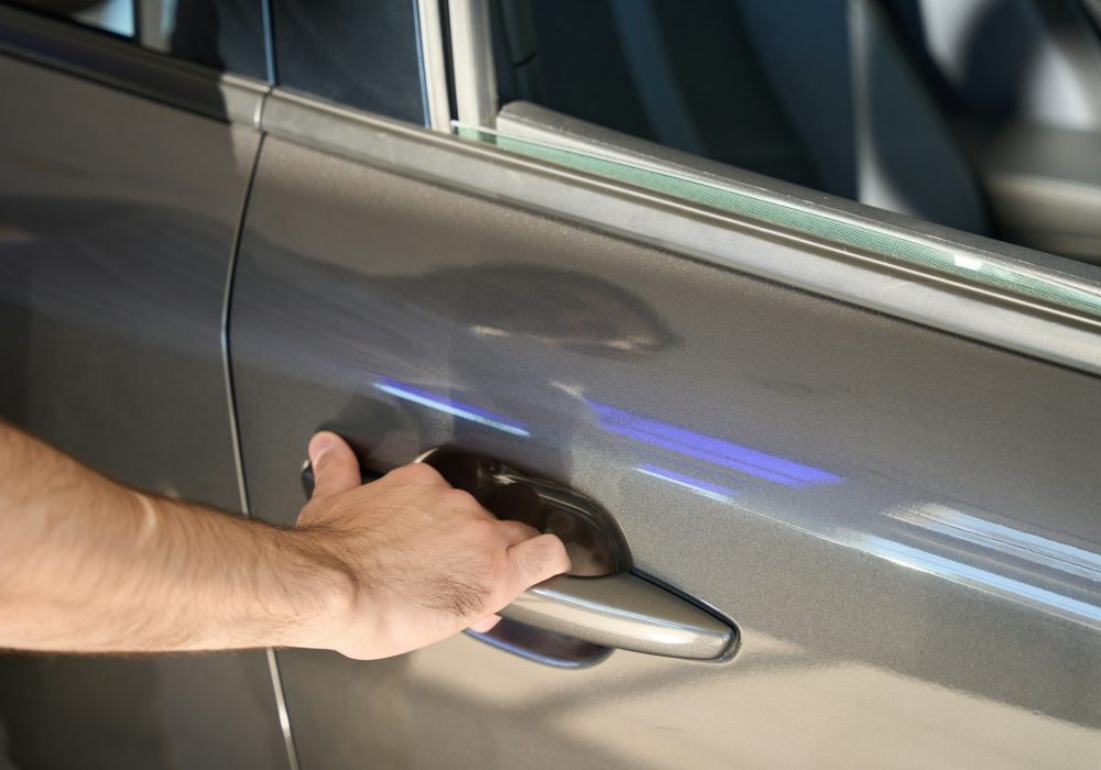 Motor vehicle owner is reaching for chrome automobile door-handle